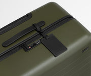 The Large suitcase in Olive Green shown shown from above highlighting TSA-approved combination lock and recycled leather luggage tag