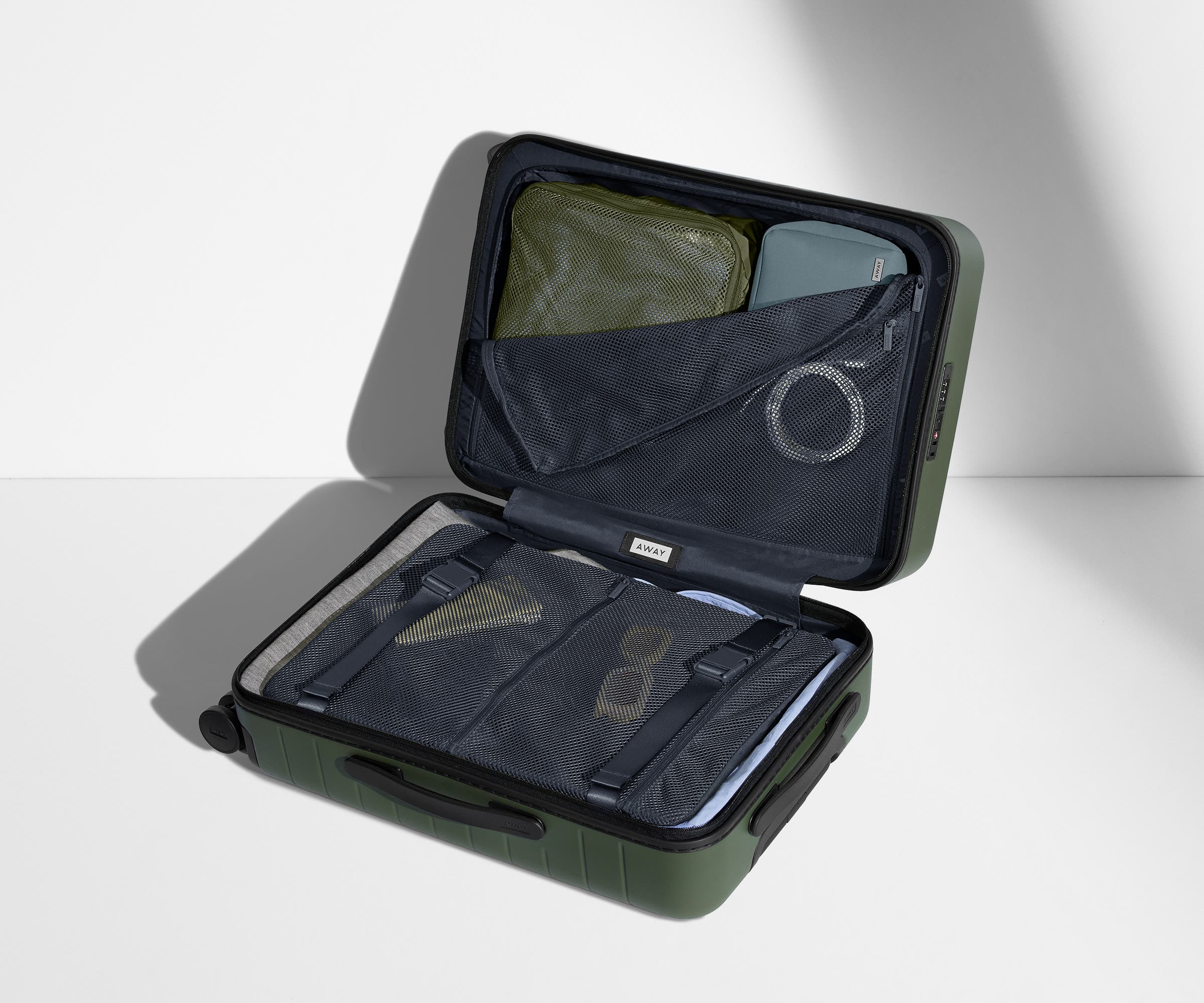 The Bigger Carry-On suitcase in Olive Green shown open on its side and packed with Away's packing organizers to show capacity and the interior compression system, designed to help you pack more in