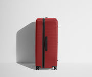 Side product view of The Trunk suitcase in Tango Red to show the slimmer top lid and deeper main compartment for easy access and packing