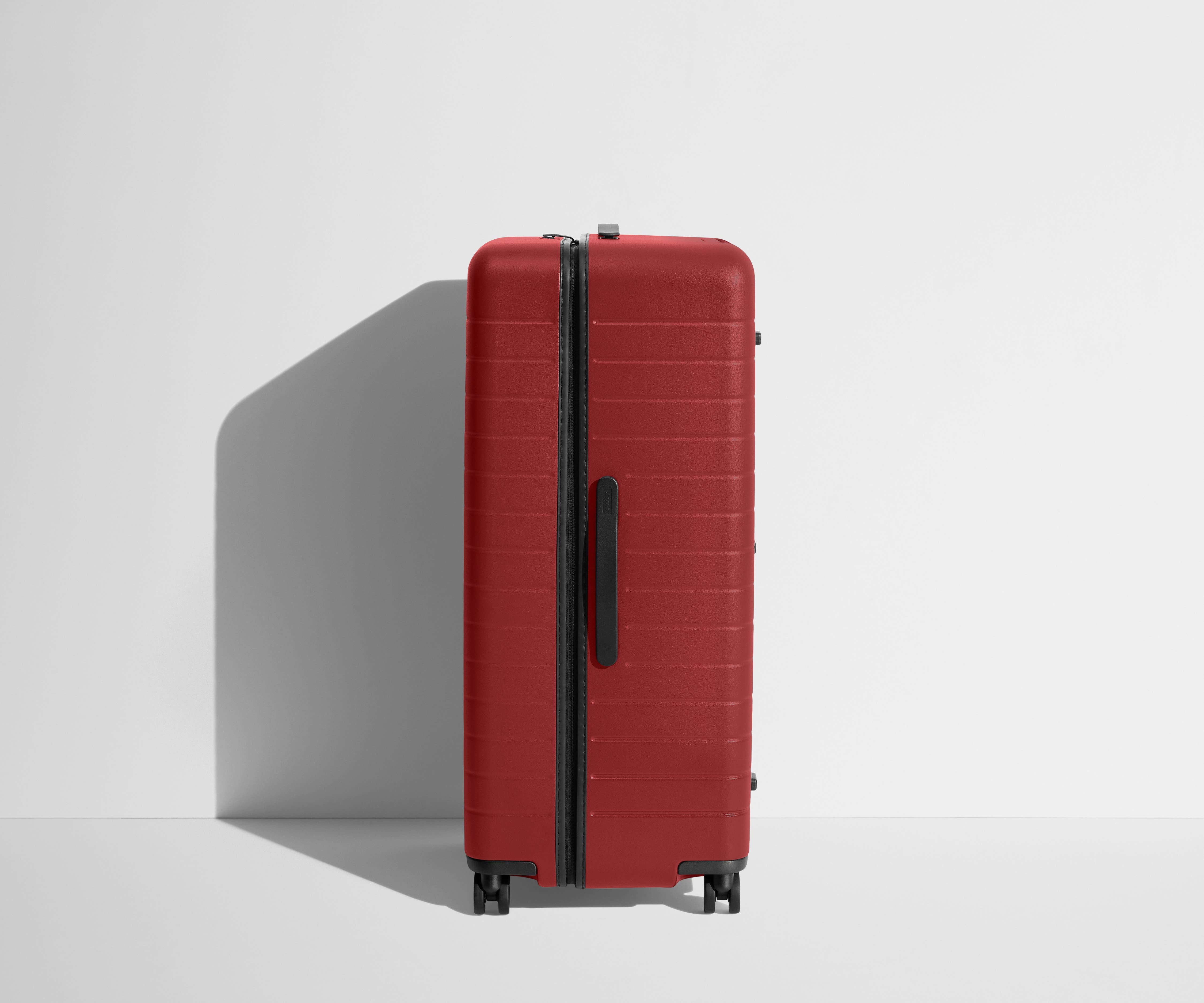 Side product view of The Trunk suitcase in Tango Red to show the slimmer top lid and deeper main compartment for easy access and packing
