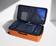 The Trunk suitcase in Sorbet Orange shown open on its side and packed with Away's packing organizers to show capacity and the interior compression system, designed to help you pack more in