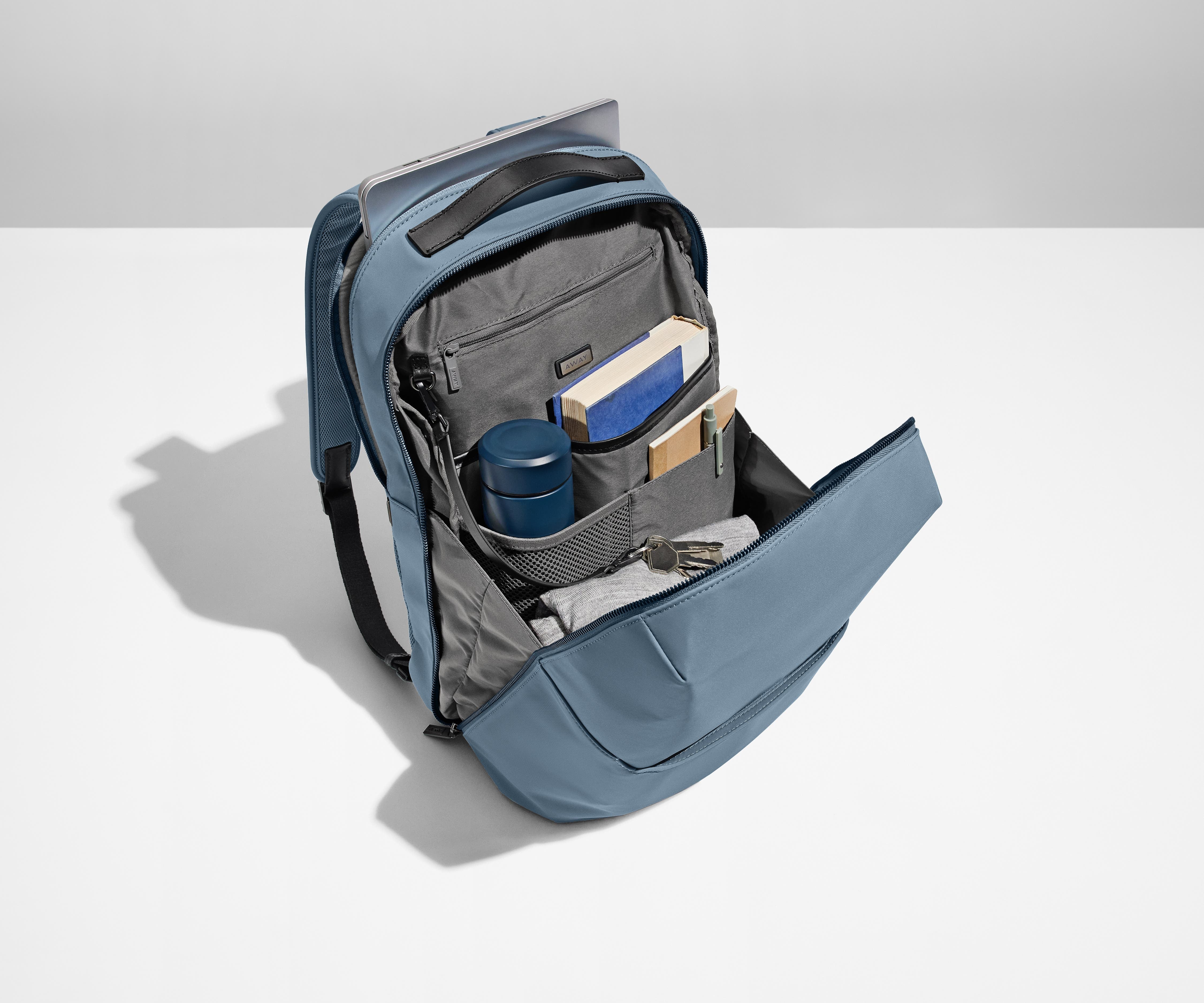 Everywhere Zip Backpack main compartment packed with a water bottle, book, notebook, and key attached to the interior key leash. A laptop is packed into the exterior laptop pocket