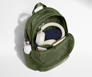 Green backpack with items like a bottle, mask, and headphones on a light gray background
