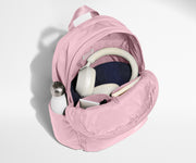 Pink backpack with a water bottle, denim item, and gray strap on a light gray background