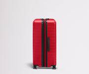 Red suitcase with black handle and wheels on a light gray background