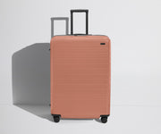 Front product view of The Large Flex suitcase in Clay Pink with raised handle