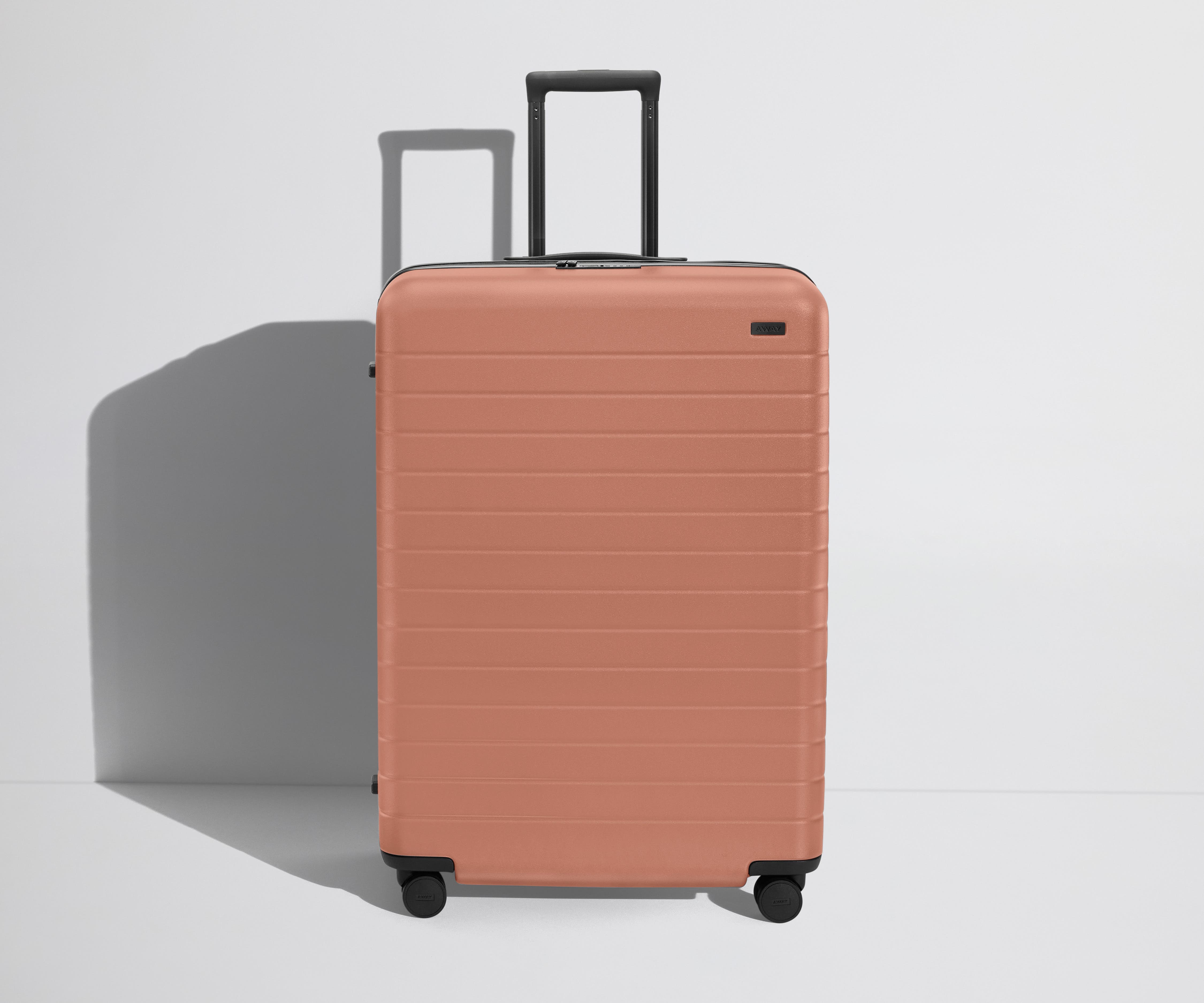 Front product view of The Large Flex suitcase in Clay Pink with raised handle