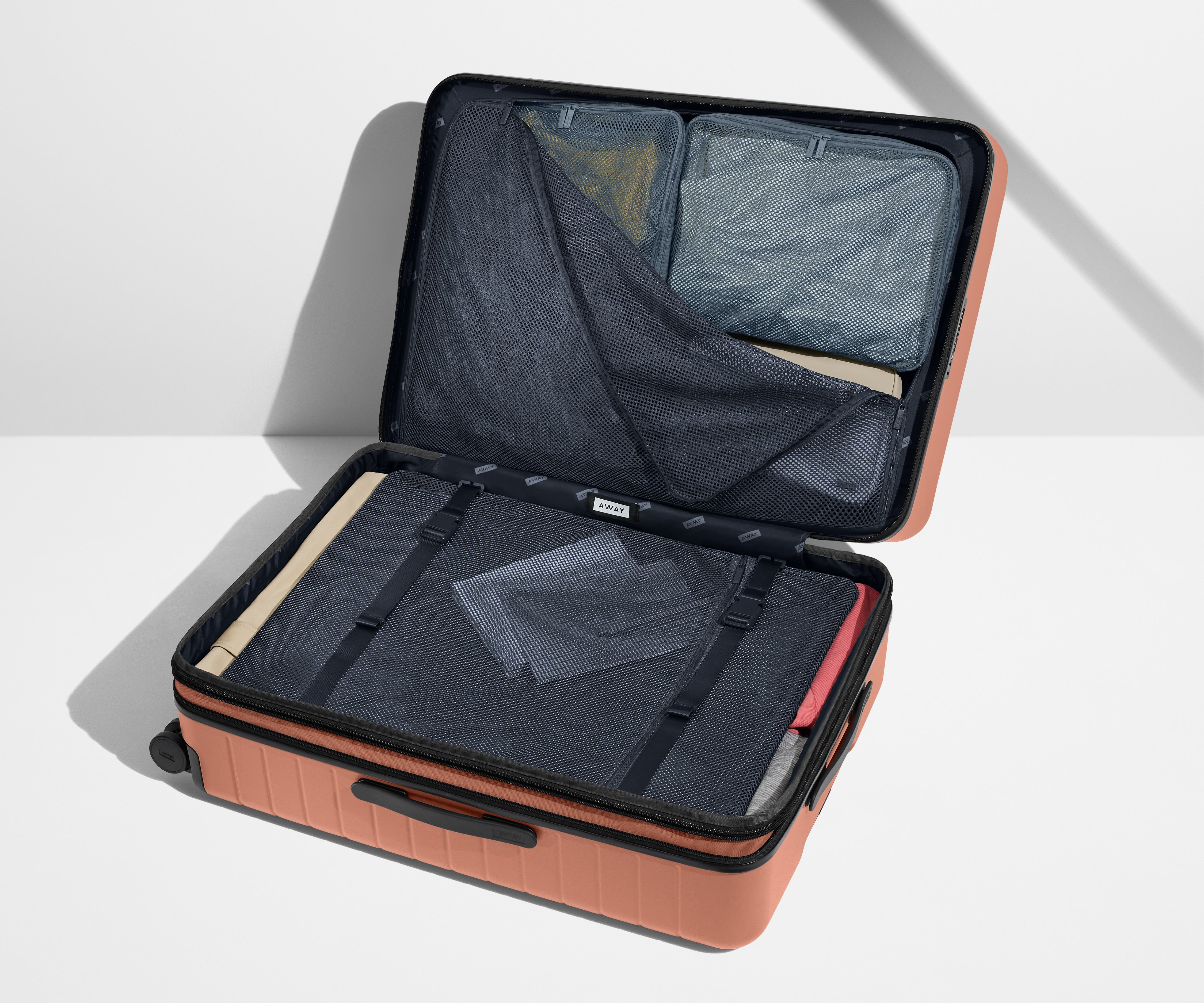 The Large Flex suitcase in Clay Pink shown open on its side and packed with Away's packing organizers to show capacity and the interior compression system, designed to help you pack more in