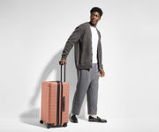 Male-presenting person standing next to a Medium Flex suitcase for scale