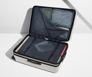 The Large Flex suitcase in Cloud Gray shown open on its side and packed with Away's packing organizers to show capacity and the interior compression system, designed to help you pack more in