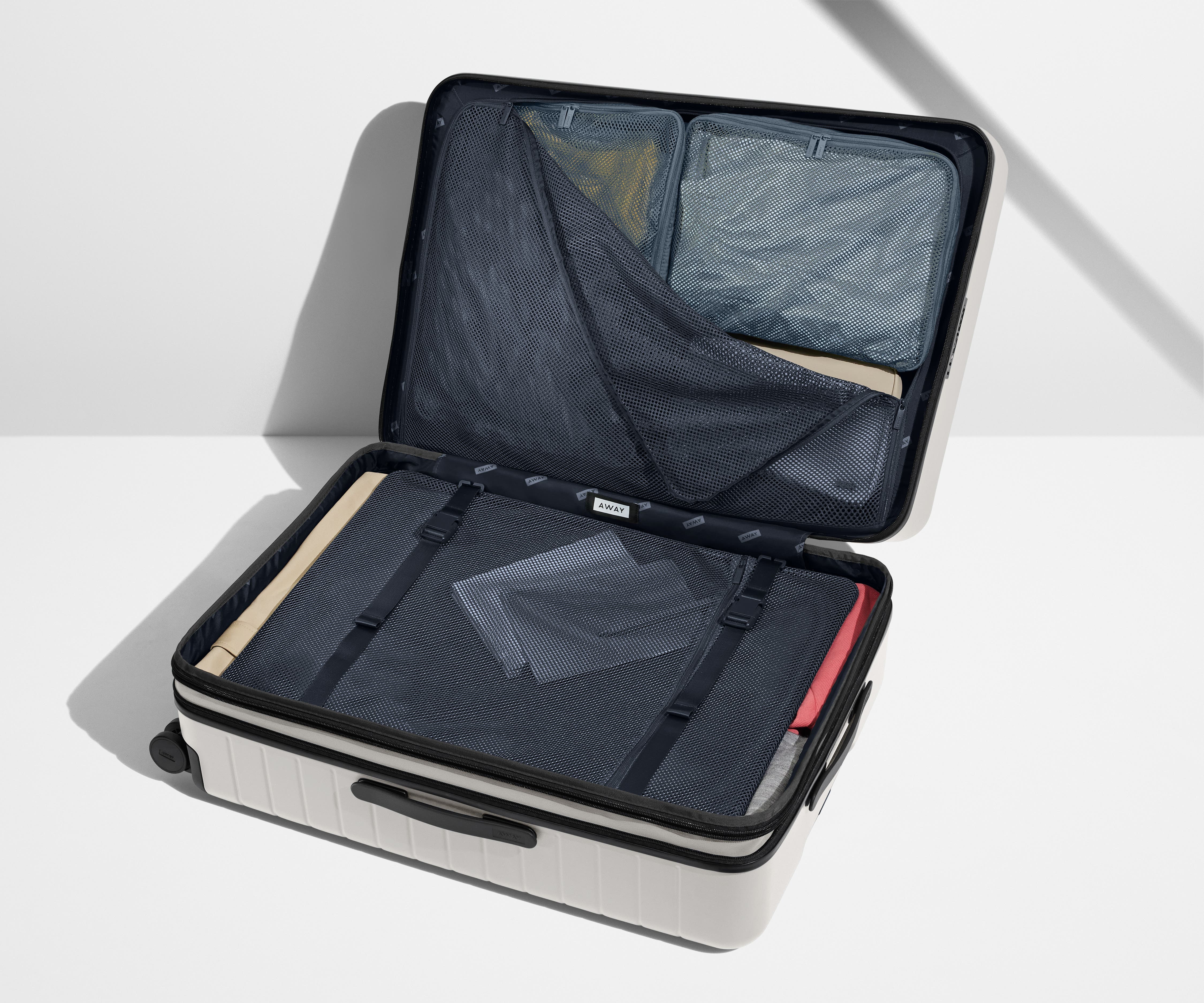 The Large Flex suitcase in Cloud Gray shown open on its side and packed with Away's packing organizers to show capacity and the interior compression system, designed to help you pack more in