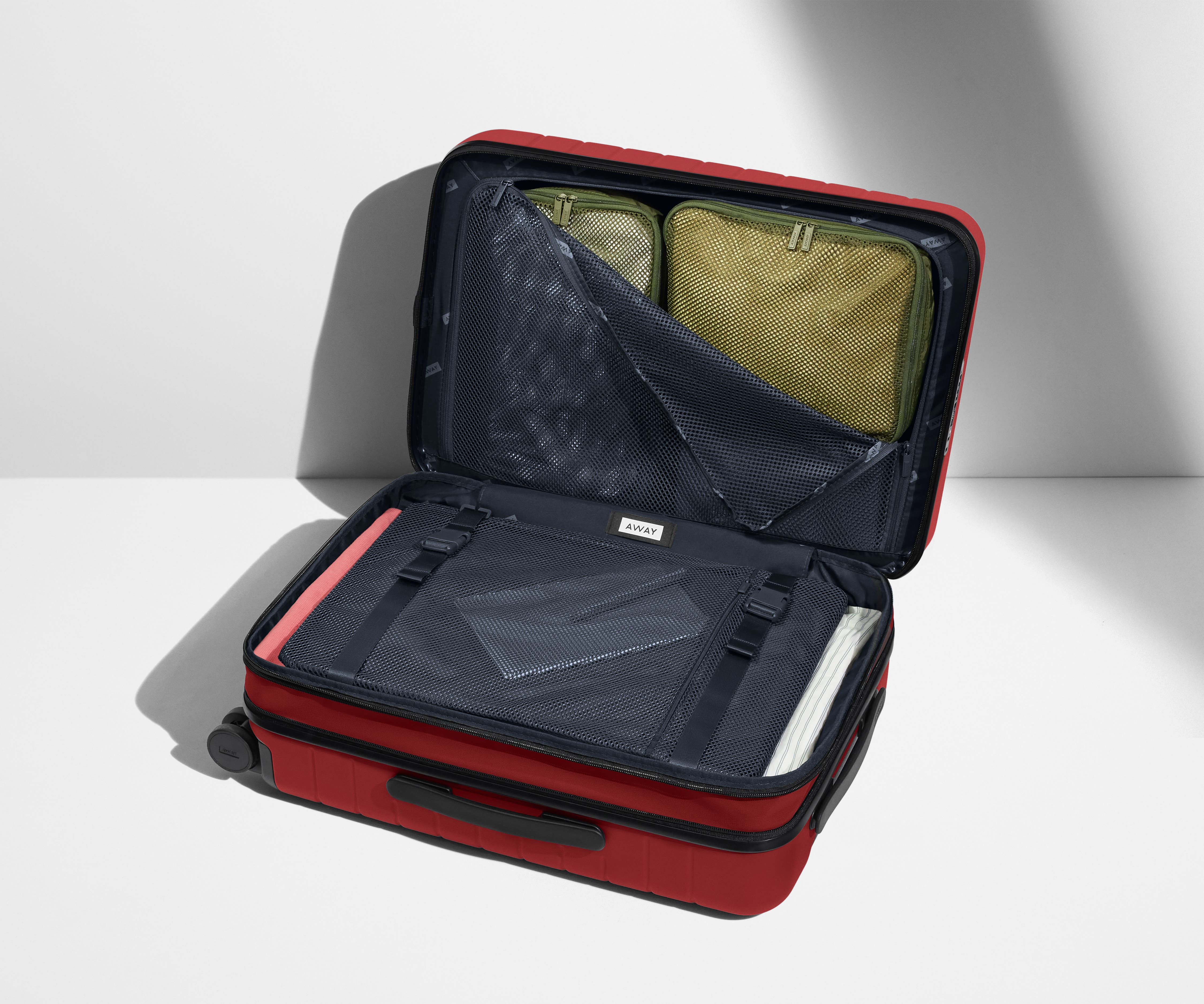 The Bigger Carry-On Flex suitcase in Tango Red shown open on its side and packed with Away's packing organizers to show capacity and the interior compression system, designed to help you pack more in