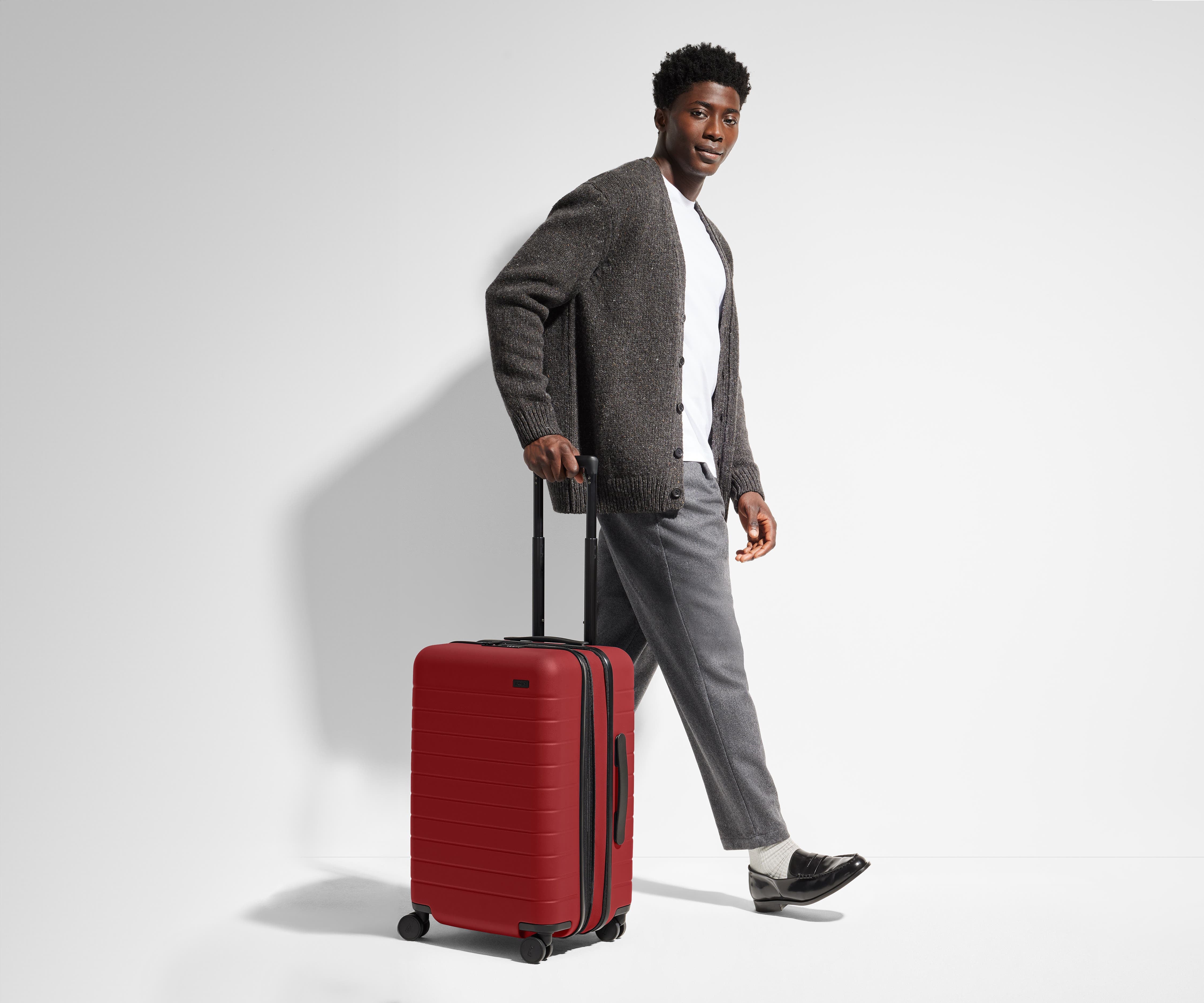 A 6'1" male model is standing next to and walking with The Bigger Carry-On suitcase by holding the raised handle to show size and scale