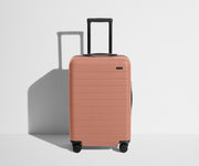 Front product view of The Bigger Carry-On suitcase in Clay Pink with raised handle
