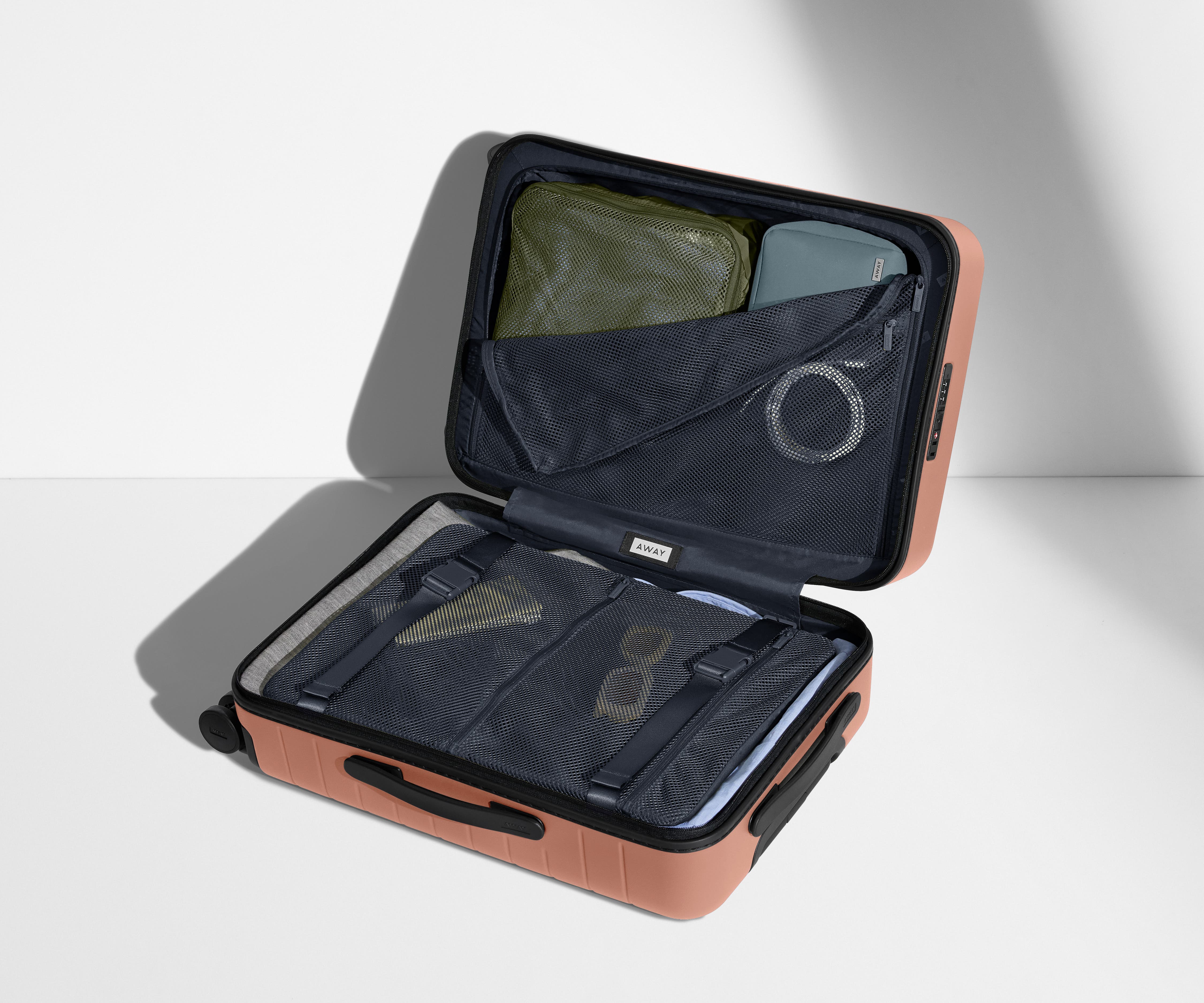 The Bigger Carry-On suitcase in Clay Pink shown open on its side and packed with Away's packing organizers to show capacity and the interior compression system, designed to help you pack more in