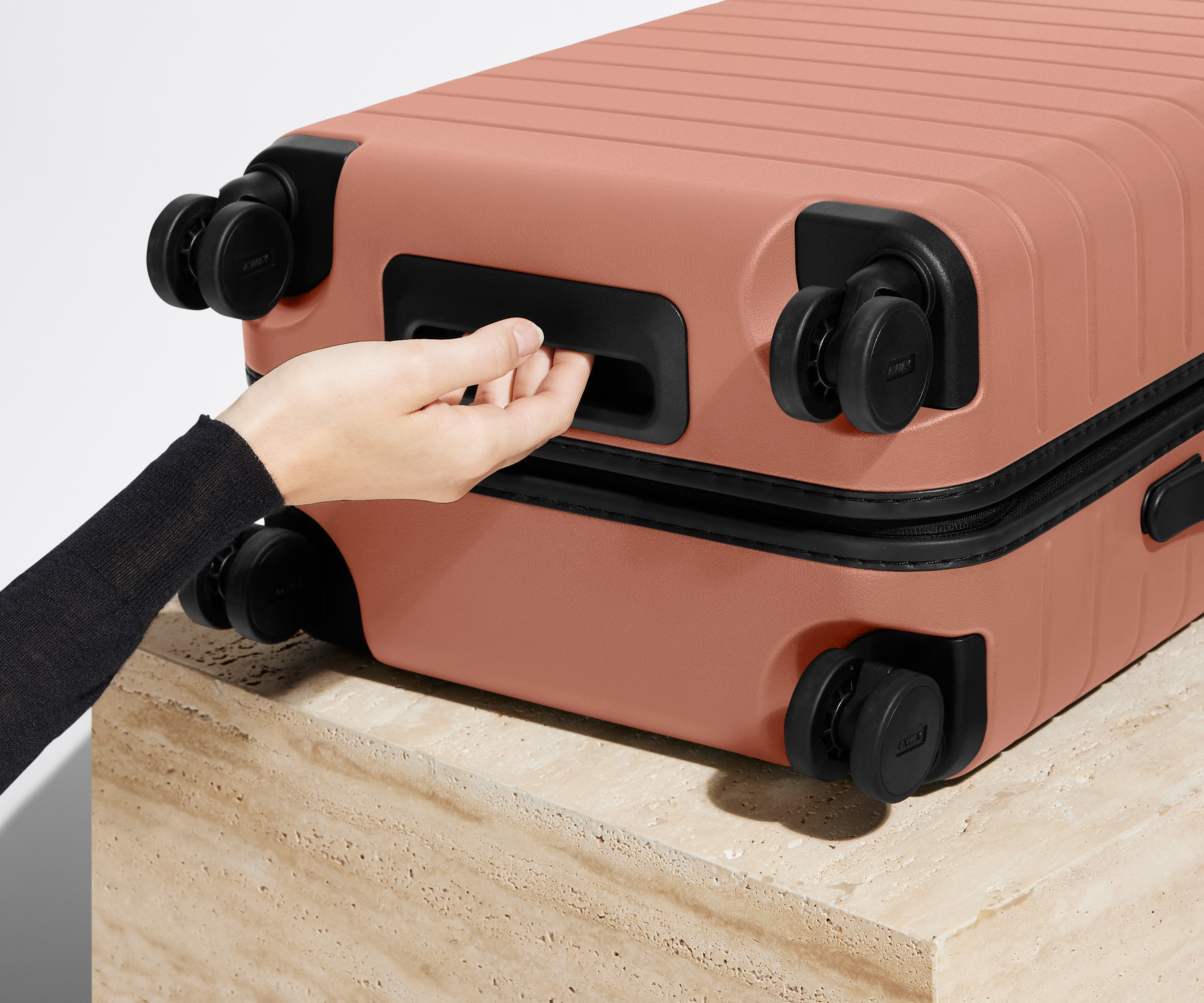 The Carry-On suitcase in Clay Pink shown from below highlighting the underside grab handle