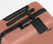The Bigger Carry-On suitcase in Clay Pink shown shown from above highlighting TSA-approved combination lock and recycled leather luggage tag