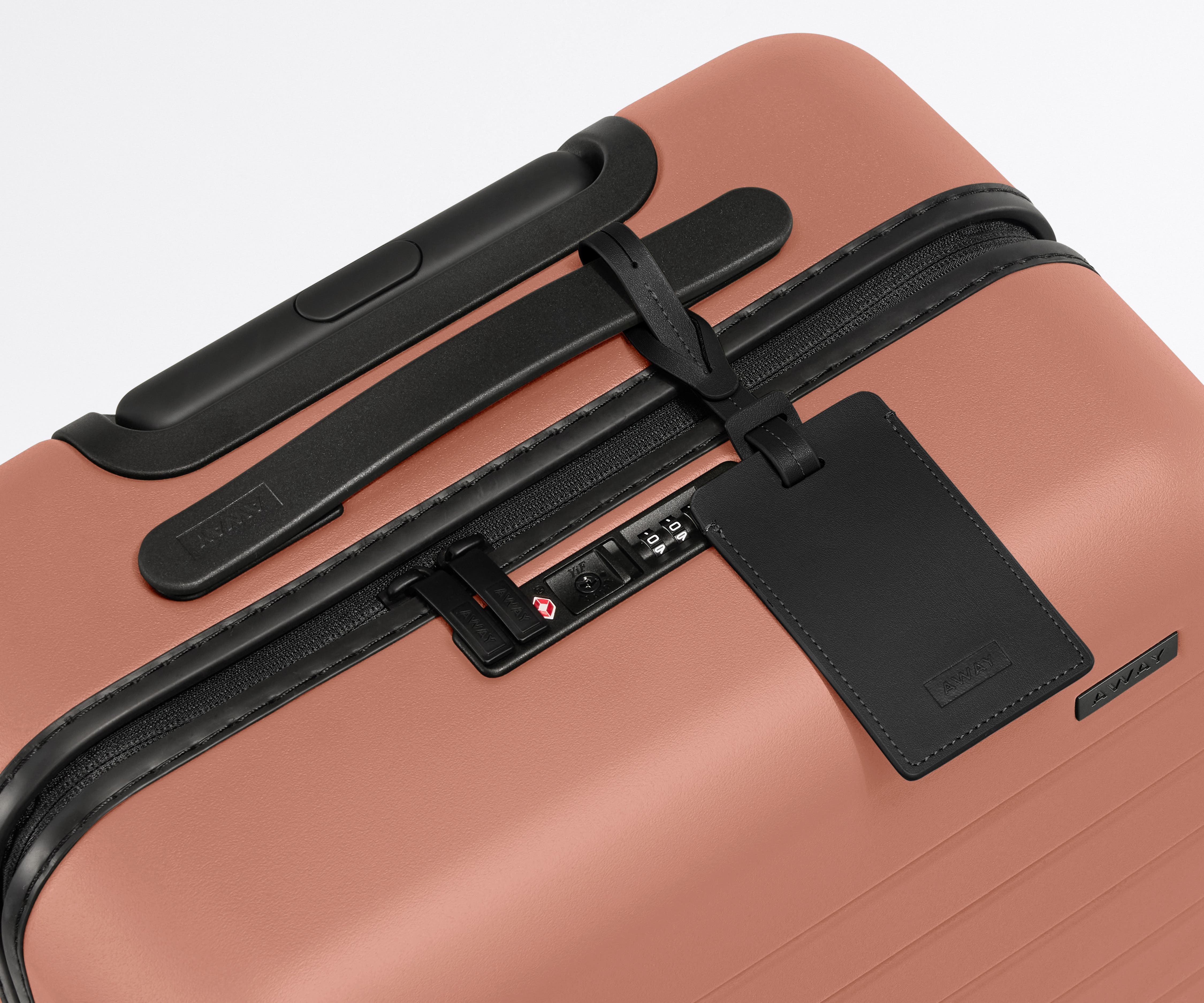 The Carry-On suitcase in Clay Pink shown shown from above highlighting TSA-approved combination lock and recycled leather luggage tag