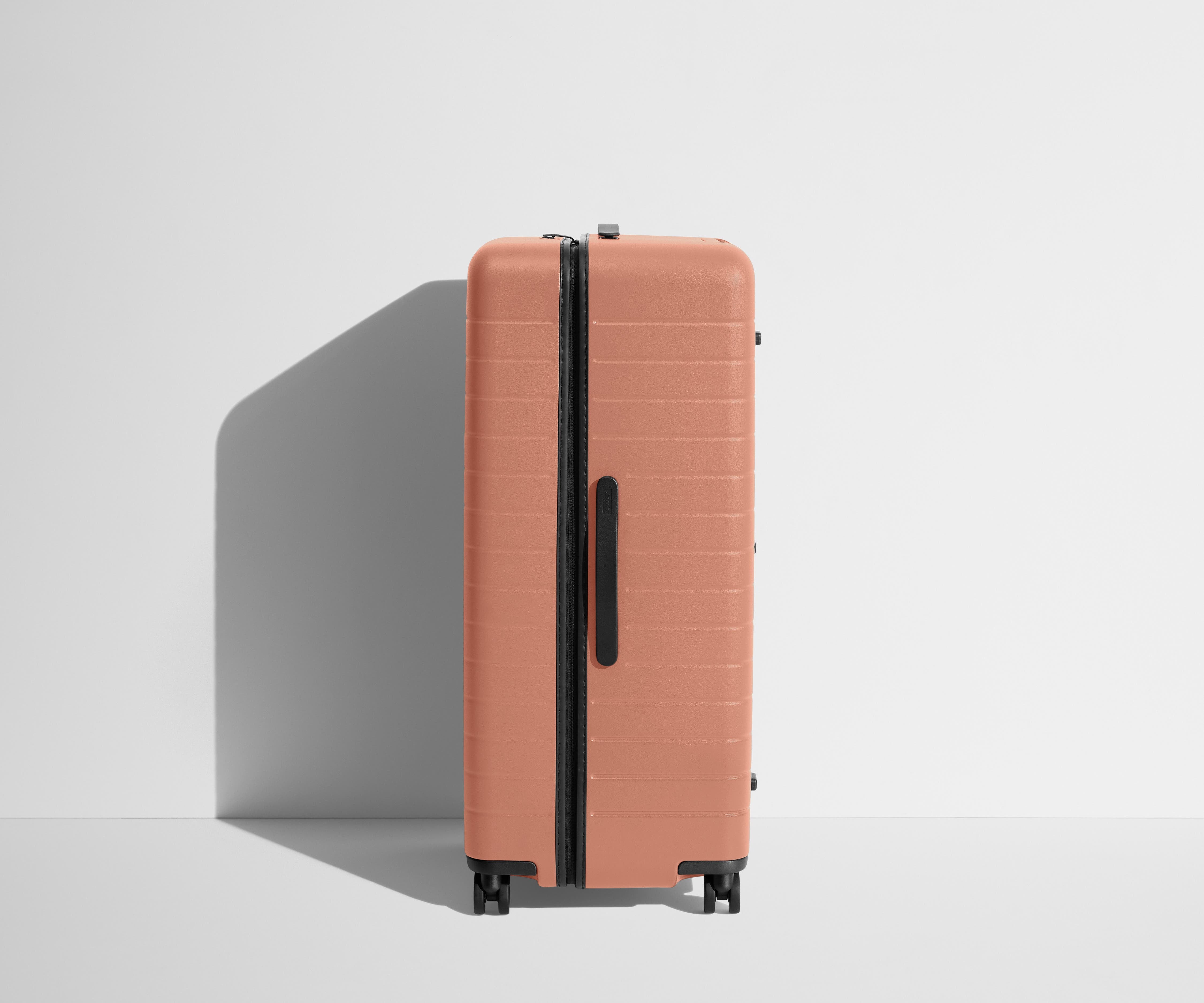 Side product view of The Trunk suitcase in Clay Pink to show the slimmer top lid and deeper main compartment for easy access and packing