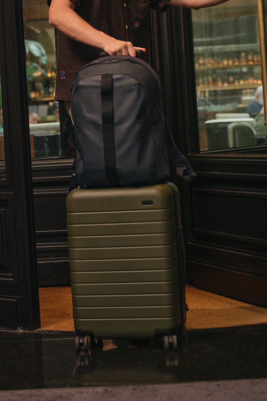 Person holding a backpack on top of a suitcase in a doorway.