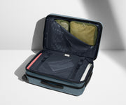 The Bigger Carry-On Flex suitcase in Coast Blue shown open on its side and packed with Away's packing organizers to show capacity and the interior compression system, designed to help you pack more in