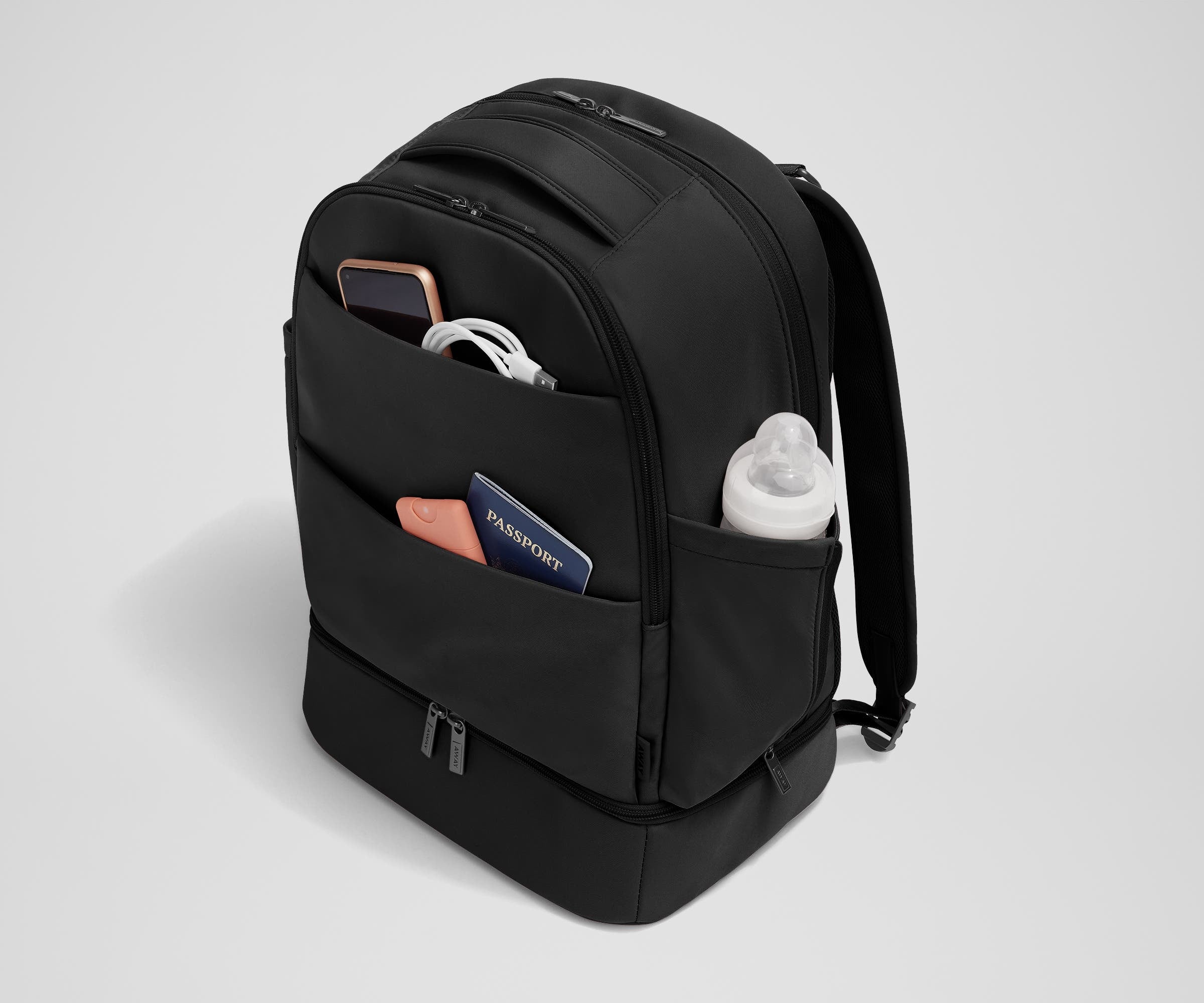 Exterior front pockets packed with travel essentials like a passport and phone, and the exterior bottle pocket packed with a milk bottle
