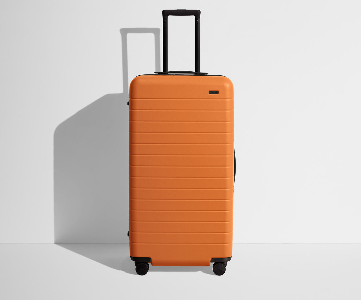 Front product view of The Trunk suitcase in Sorbet Orange with raised handle