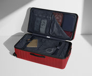 The Trunk suitcase in Tango Red shown open on its side and packed with Away's packing organizers to show capacity and the interior compression system, designed to help you pack more in