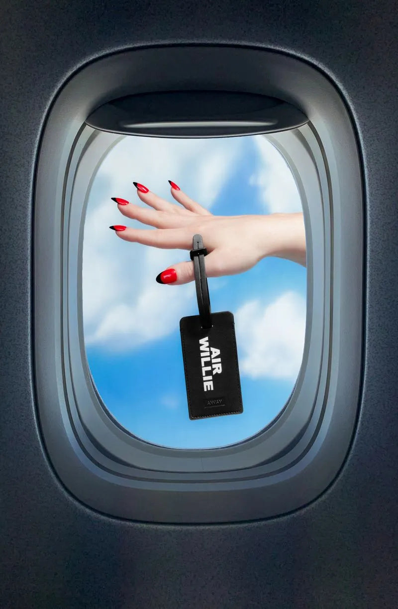 a woman holding an Away luggage tag outside of a plane window with clouds in the background