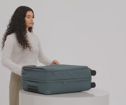 A female model filling The Softside Medium suitcase in Coast Blue with Away's packing organizers and using the interior organization and compression system for seamless packing